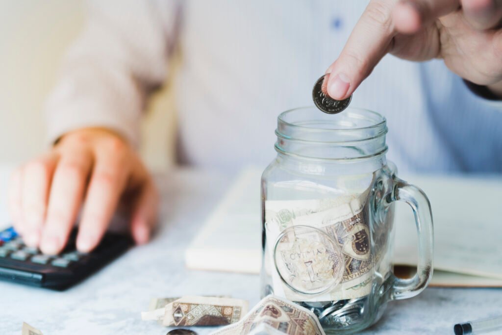 Saving vs Investing for Beginners: What’s the Difference? hand putting coin inside jar